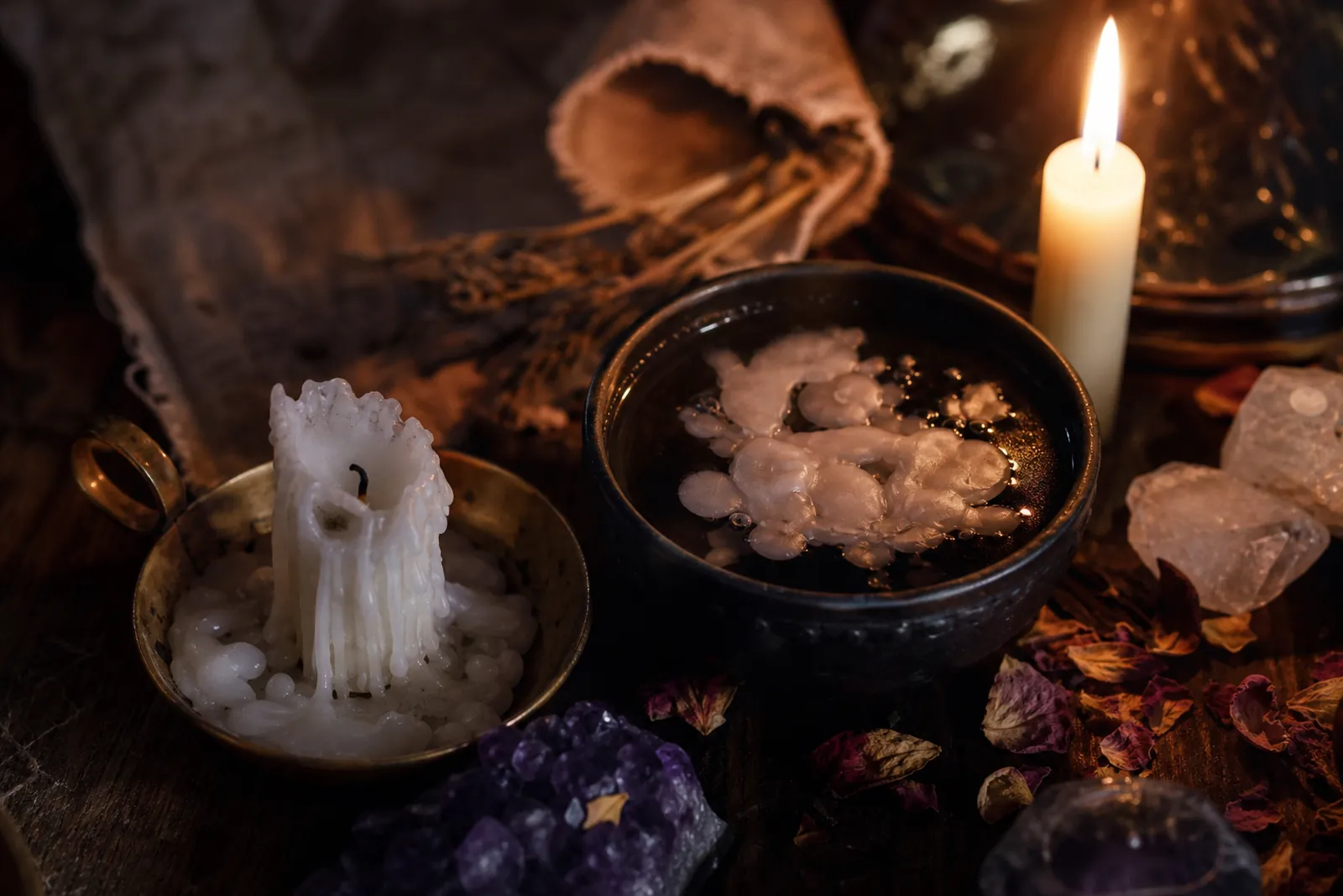 A burned-down candle with melted wax drips beside a bowl of water holding floating wax shapes